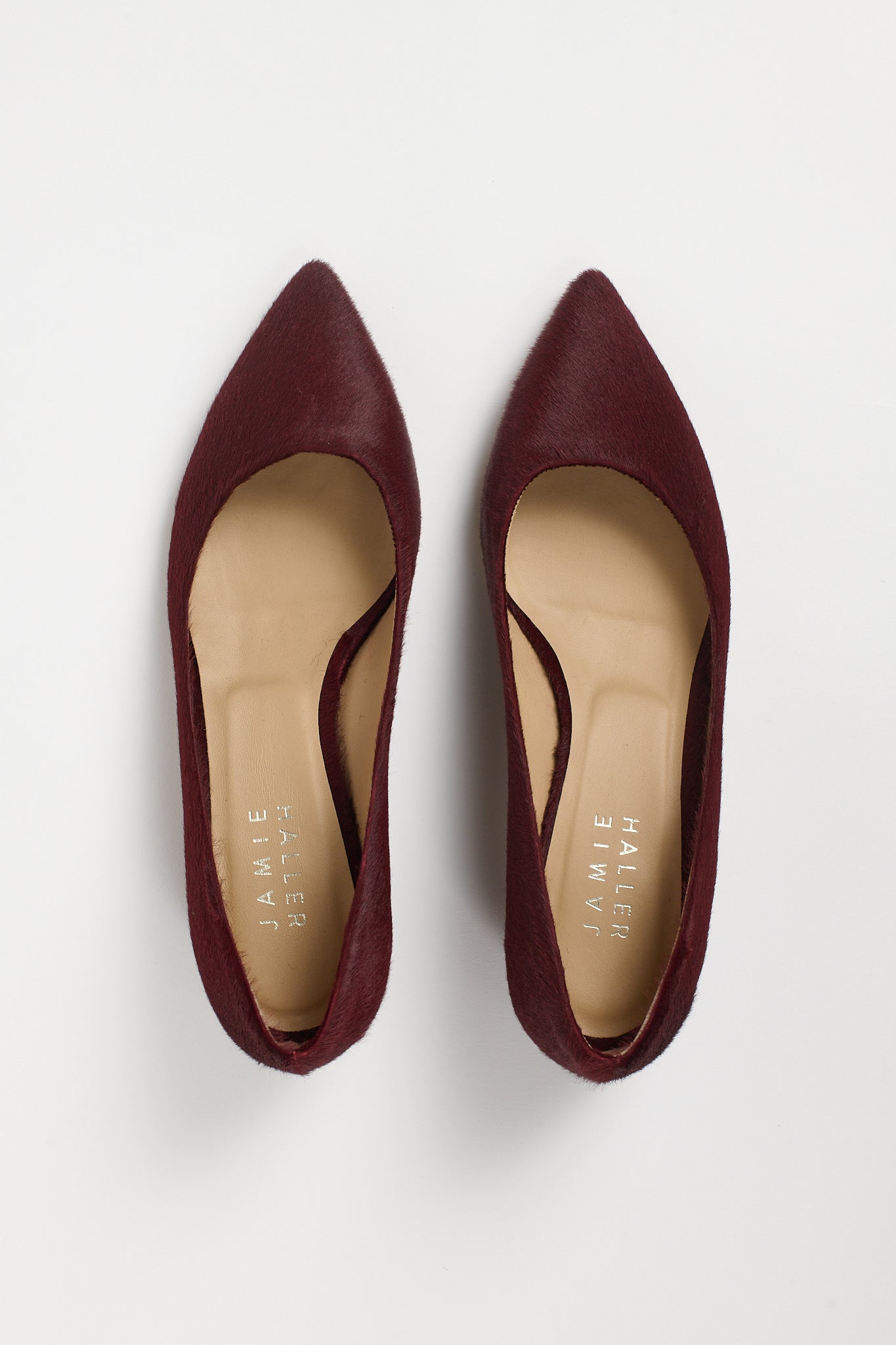 A pair of pointed-toe flat shoes in burgundy suede, shown from a top-down view on a light gray background. The insoles are beige with the brand name 'JAMIE HALLER' printed vertically.
