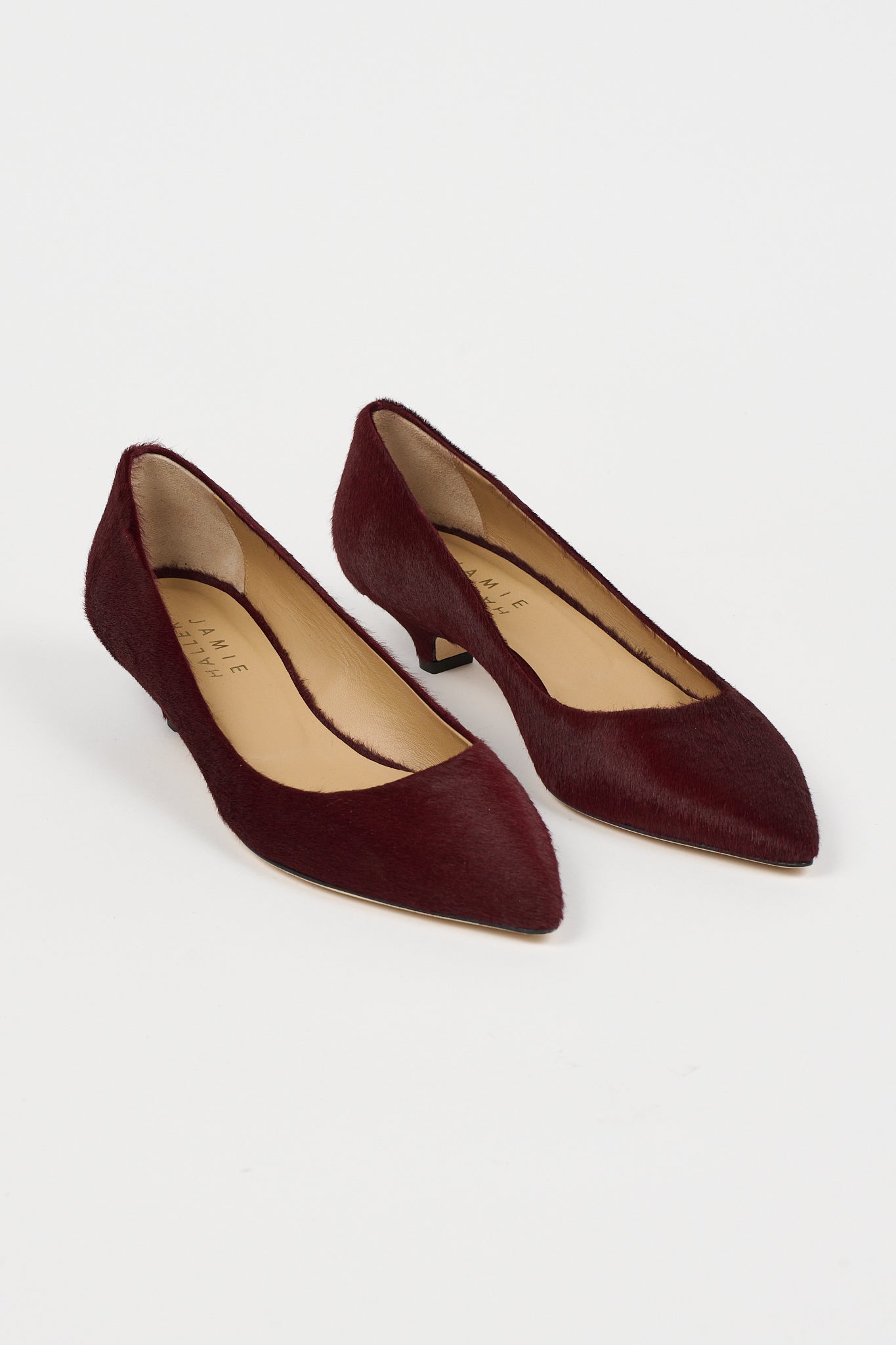 A pair of pointed-toe low-heel pumps in deep burgundy suede, shown from a high-angle view on a clean white background. The brand name 'Jamie Haller' is visible on the beige insoles.