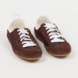 A pair of dark brown suede slip-on sneakers with white laces and a white plush lining, displayed on a clean white background.