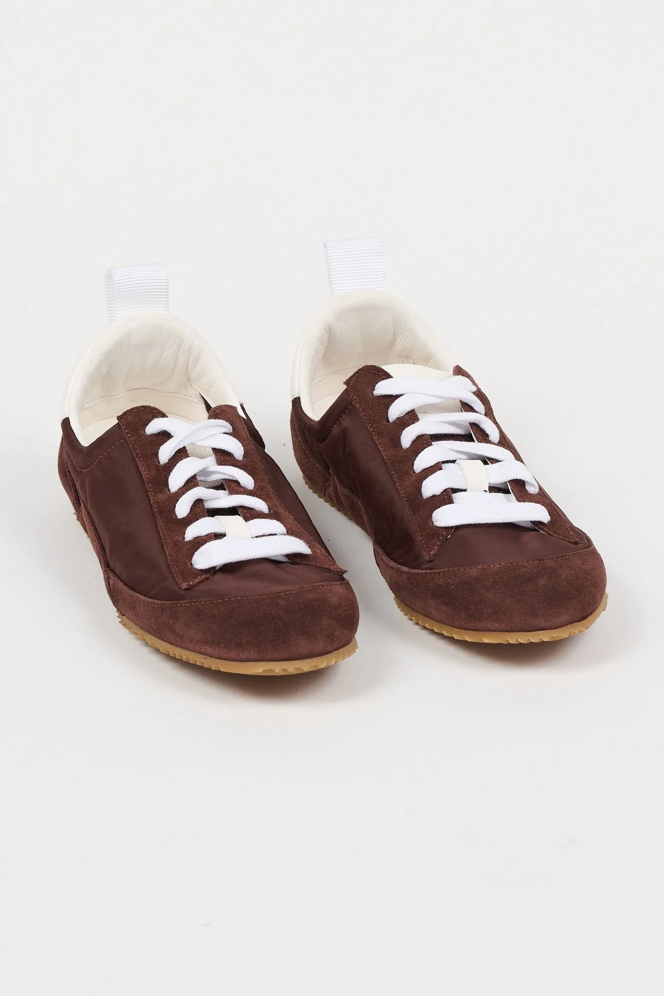 A pair of dark brown suede slip-on sneakers with white laces and a white plush lining, displayed on a clean white background.