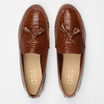 A pair of brown crocodile-embossed tassel loafers shown from a top-down view on a light gray background. The brand name 'JAMIE HALLER' is printed on the tan insoles.