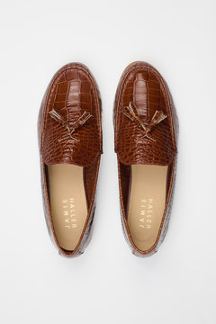 A pair of brown crocodile-embossed tassel loafers shown from a top-down view on a light gray background. The brand name 'JAMIE HALLER' is printed on the tan insoles.