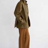 A model is shown in profile wearing an olive green jacket, camel brown wide-leg trousers, and dark brown leather boots against a clean white studio background.
