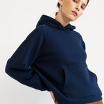 A model wearing a navy blue oversized hoodie, a brown pleated wide-leg skirt, and red shoes, standing against a plain white studio background.