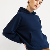 A model wearing a navy blue oversized hoodie, a brown pleated wide-leg skirt, and red shoes, standing against a plain white studio background.