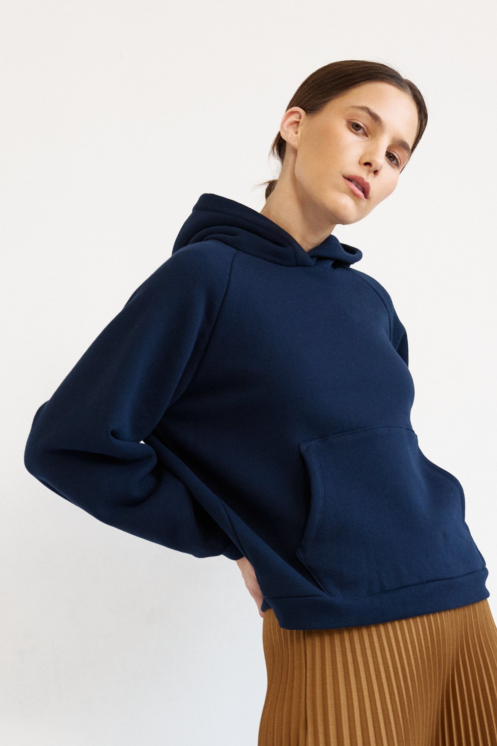 A model wearing a navy blue oversized hoodie, a brown pleated wide-leg skirt, and red shoes, standing against a plain white studio background.