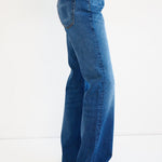 A person wearing a pair of high-waisted, wide-leg blue denim jeans, shown from the waist down against a plain white studio background.