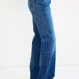A person wearing a pair of high-waisted, wide-leg blue denim jeans, shown from the waist down against a plain white studio background.