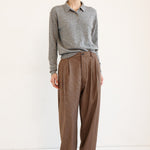 A model stands against a plain white studio background wearing a gray long-sleeve knit polo shirt and high-waisted brown wide-leg trousers.