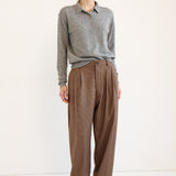 A model stands against a plain white studio background wearing a gray long-sleeve knit polo shirt and high-waisted brown wide-leg trousers.