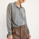 A model wearing a heather gray long-sleeve polo shirt tucked into brown patterned trousers, photographed against a plain off-white studio background.