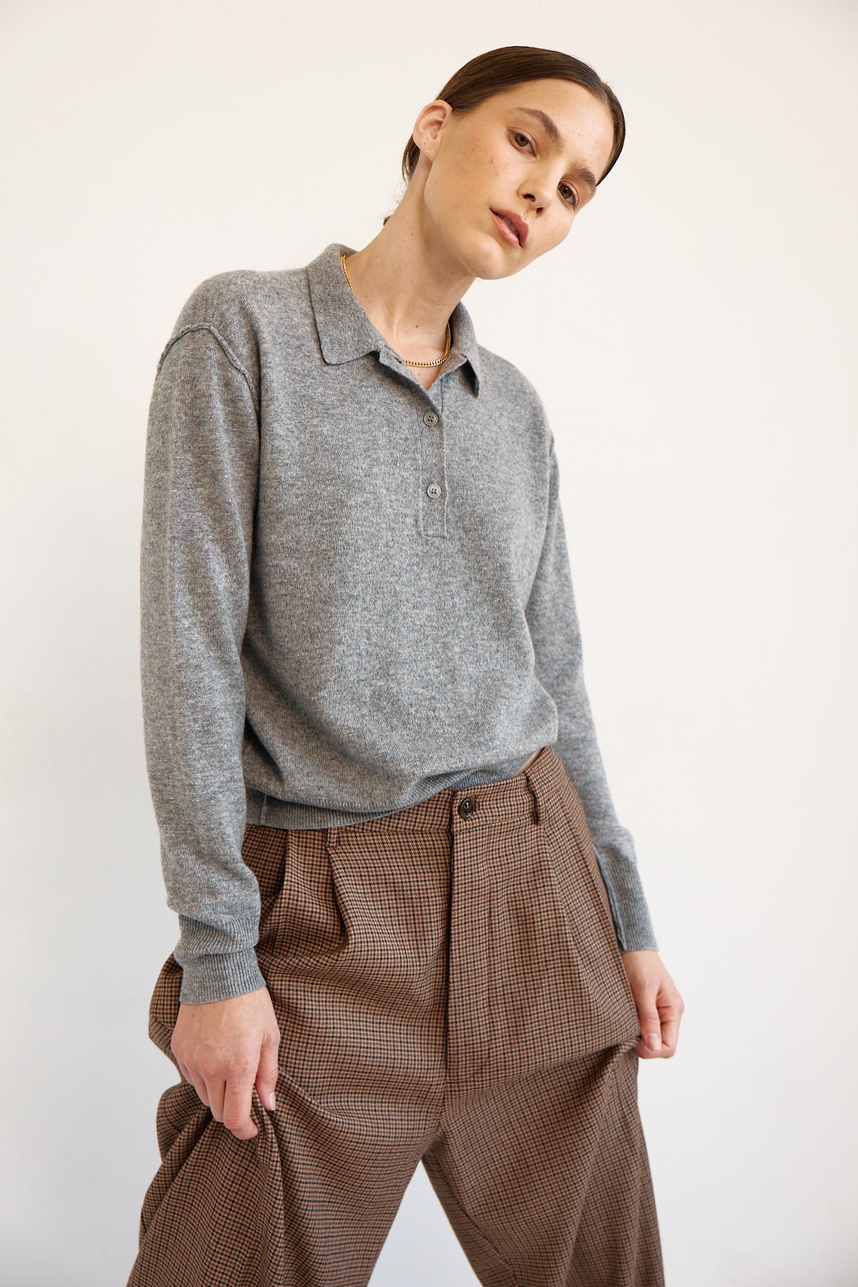 A model wearing a heather gray long-sleeve polo shirt tucked into brown patterned trousers, photographed against a plain off-white studio background.