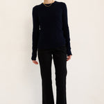 A woman modeling a dark navy long-sleeve knit top and black wide-leg trousers with black ankle boots, standing against a plain off-white studio background.