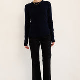 A woman modeling a dark navy long-sleeve knit top and black wide-leg trousers with black ankle boots, standing against a plain off-white studio background.