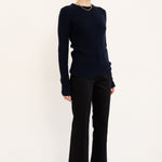 A woman modeling a dark navy long-sleeve knit sweater, black wide-leg trousers, and black pointed-toe ankle boots against a plain white studio background.