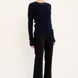 A woman modeling a dark navy long-sleeve knit sweater, black wide-leg trousers, and black pointed-toe ankle boots against a plain white studio background.