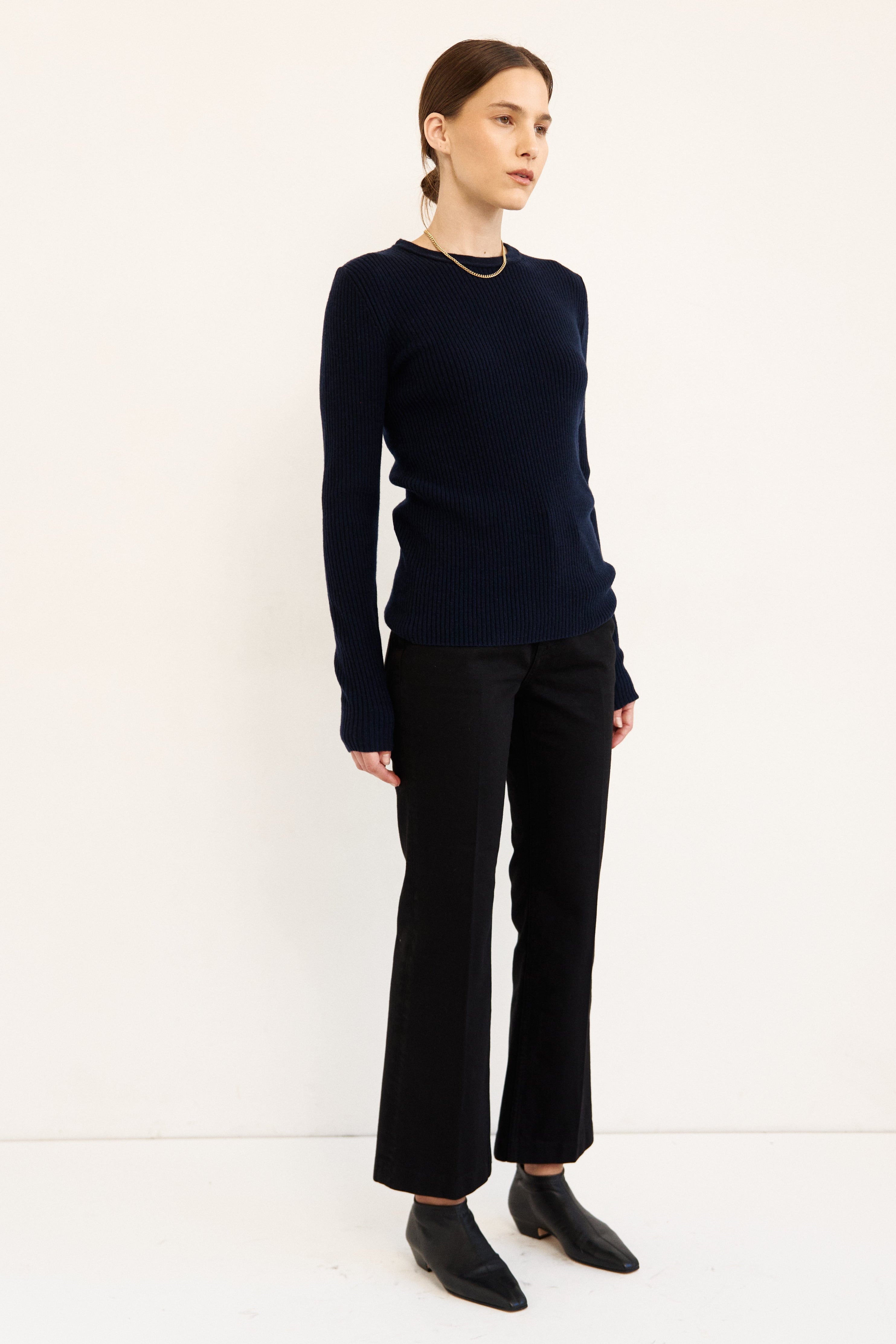 A woman modeling a dark navy long-sleeve knit sweater, black wide-leg trousers, and black pointed-toe ankle boots against a plain white studio background.