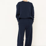 woman in navy sweatshirt and jeans in front of a white wall