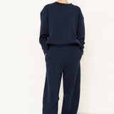 woman in navy sweatshirt and jeans in front of a white wall