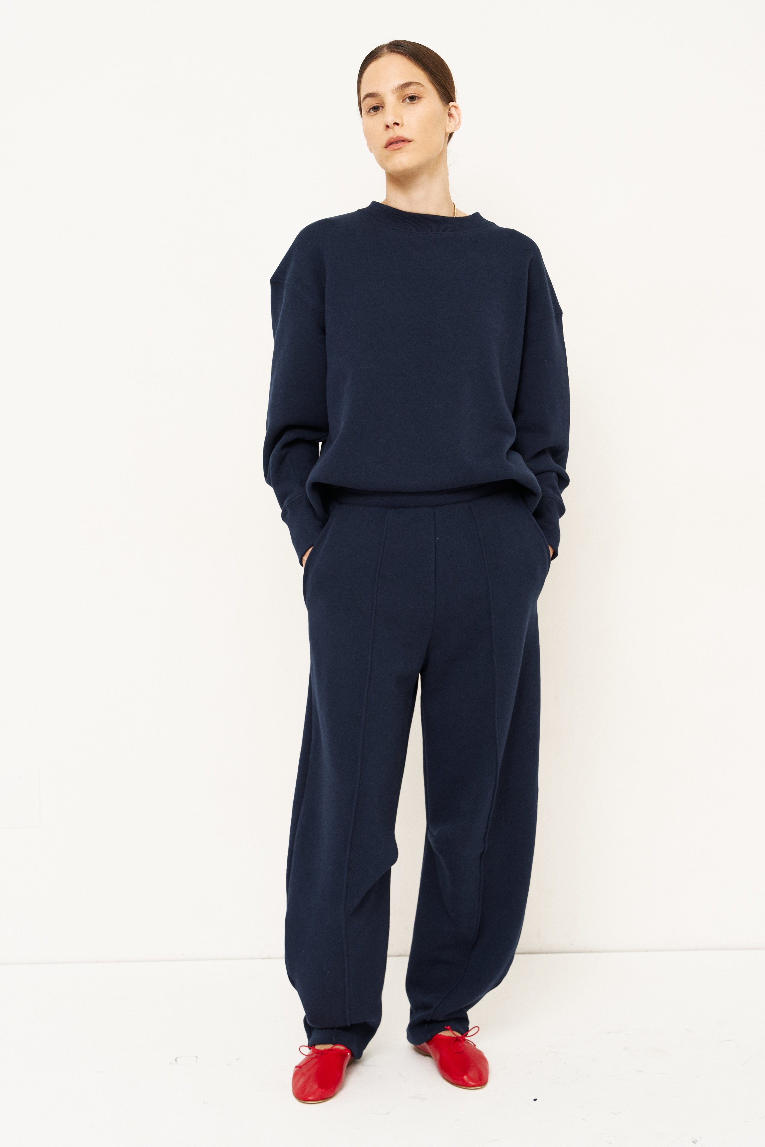 woman in navy sweatshirt and jeans in front of a white wall
