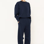 woman in navy sweatshirt and pants in front of a white wall