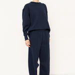 woman in navy sweatshirt and jeans in front of a white wall