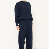 woman in navy sweatshirt and jeans in front of a white wall