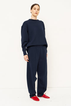 woman in navy sweatshirt and jeans in front of a white wall