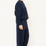 side profile of a woman standing in all navy tracksuit in front of a white wall