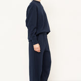 side profile of a woman standing in all navy tracksuit in front of a white wall