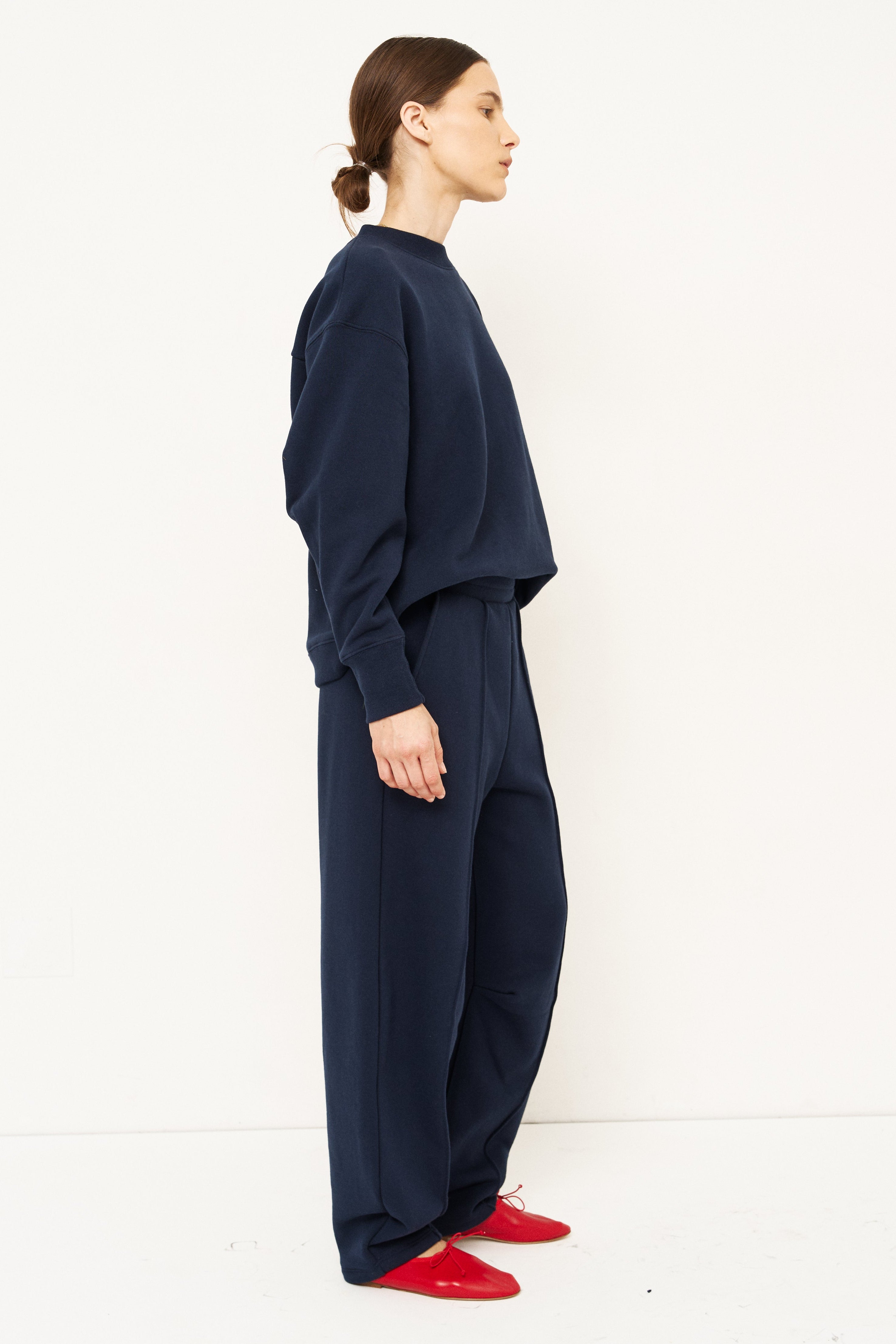 side profile of a woman standing in all navy tracksuit in front of a white wall