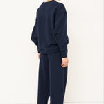 back side of woman standing in front of a white wall in a navy tracksuit