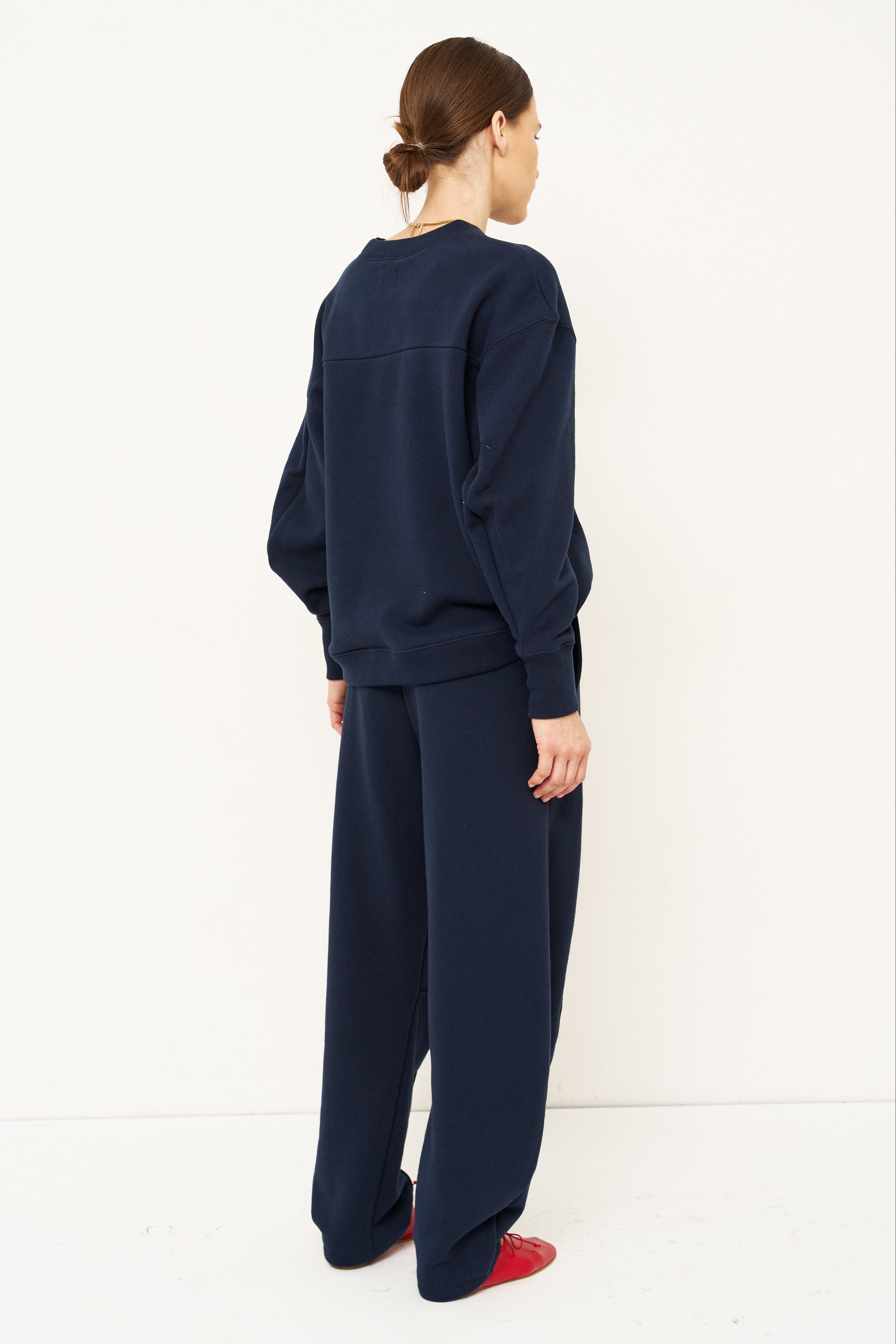 back side of woman standing in front of a white wall in a navy tracksuit