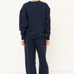 woman in navy sweatshirt and pants in front of a white wall