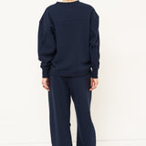 woman in navy sweatshirt and pants in front of a white wall