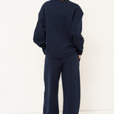 woman standing in all navy tracksuit in front of a white wall