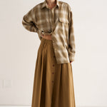 Person wearing a plaid shirt and long beige skirt on a white background