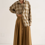 Person wearing a plaid shirt and long beige skirt on a white background