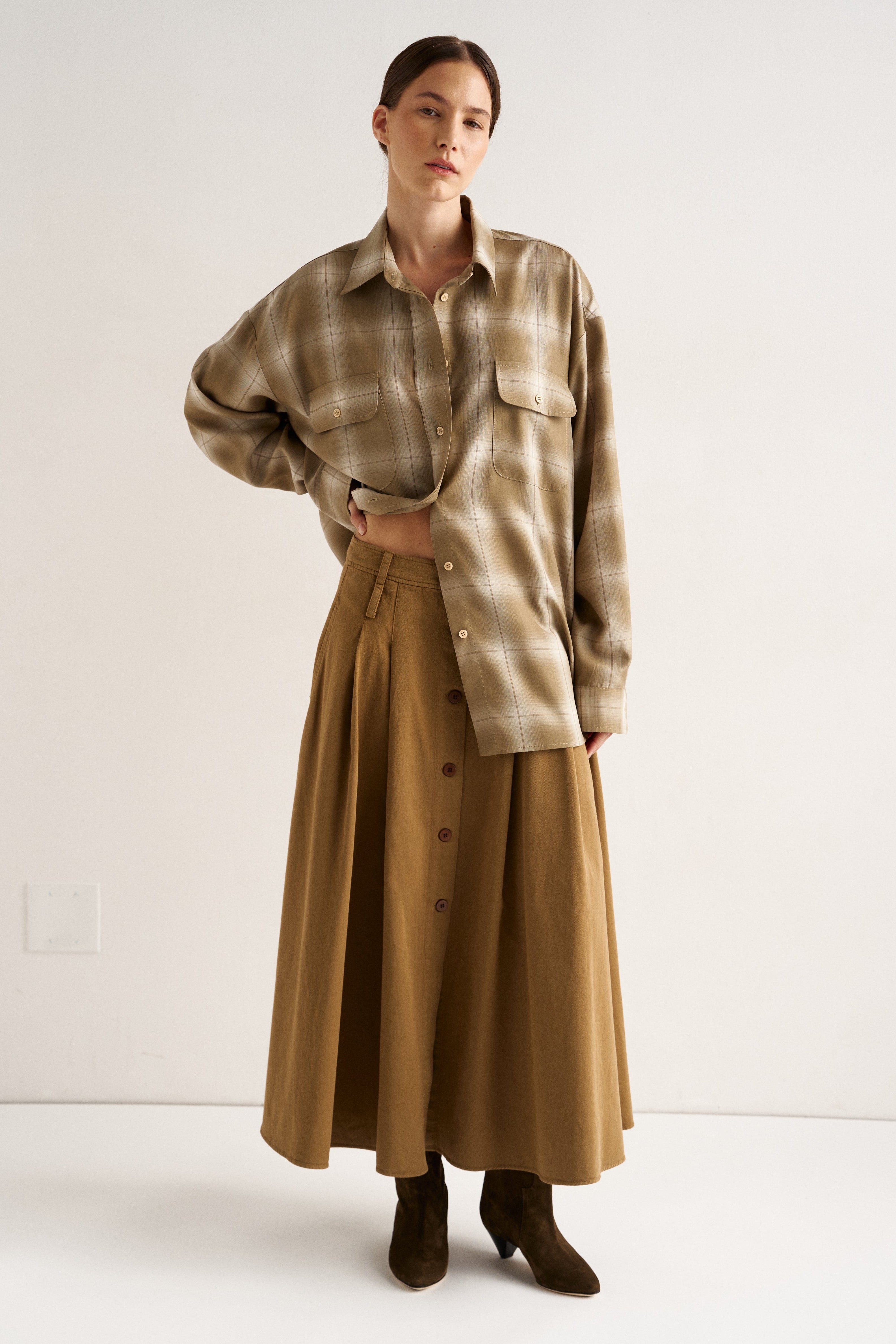 Person wearing a plaid shirt and long beige skirt on a white background