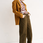 Woman wearing a mustard jacket and brown pants against a white background