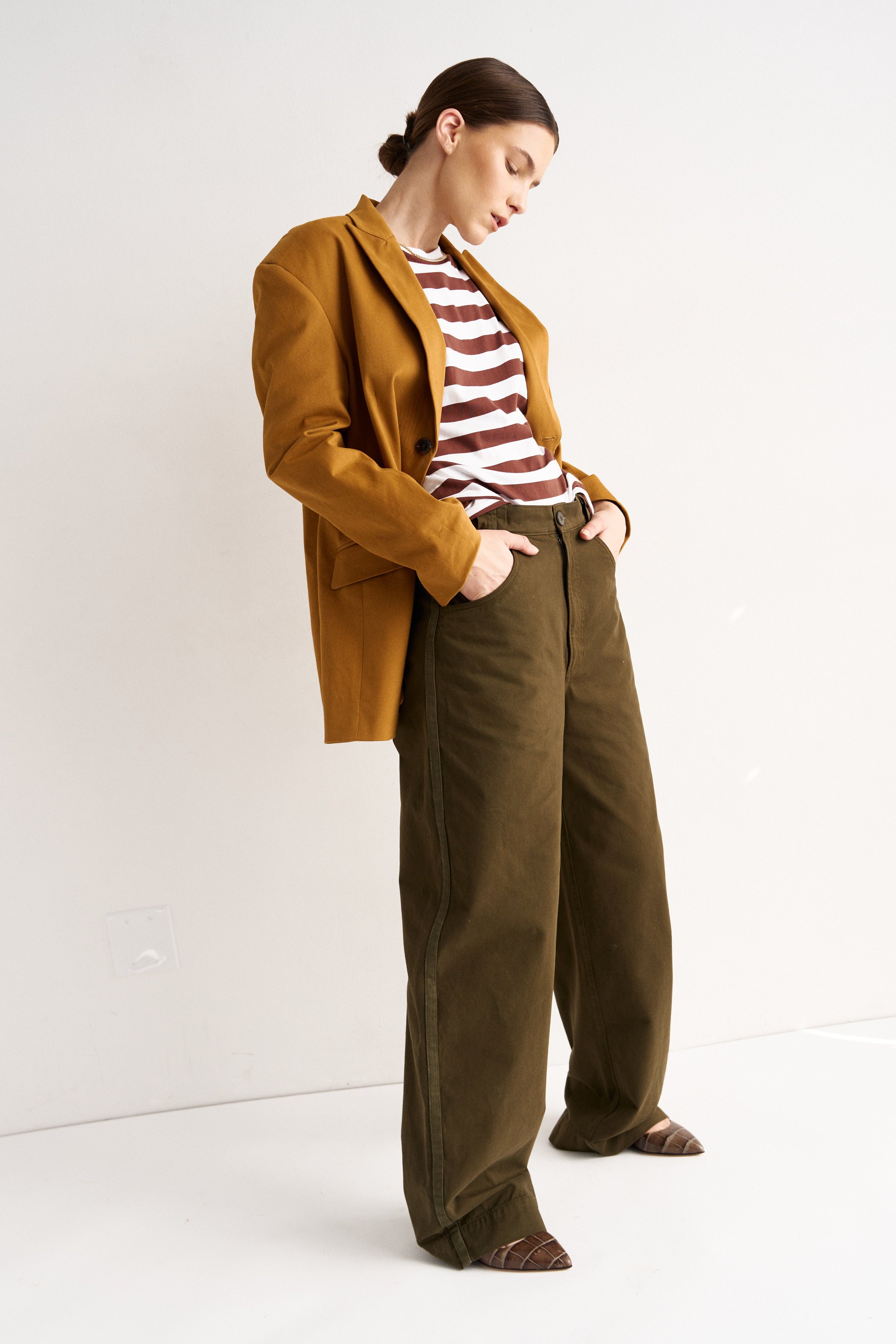 Woman wearing a mustard jacket and brown pants against a white background