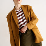 Person wearing a mustard yellow coat over a striped shirt with a neutral background