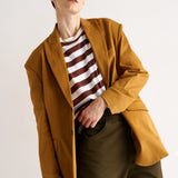 Person wearing a mustard yellow coat over a striped shirt with a neutral background