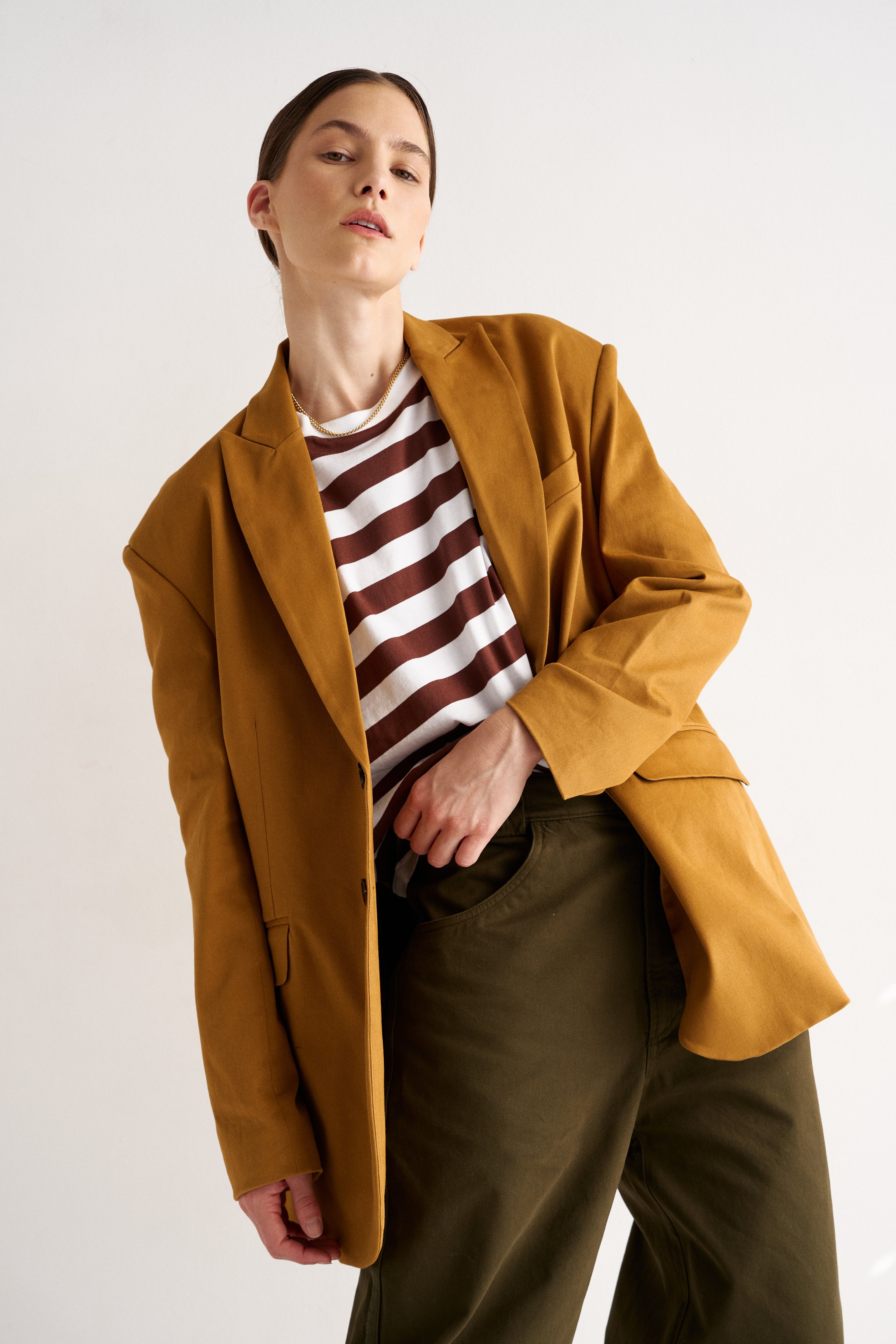 Person wearing a mustard yellow coat over a striped shirt with a neutral background