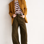 Person wearing a mustard yellow coat, striped shirt, and green pants on a white background