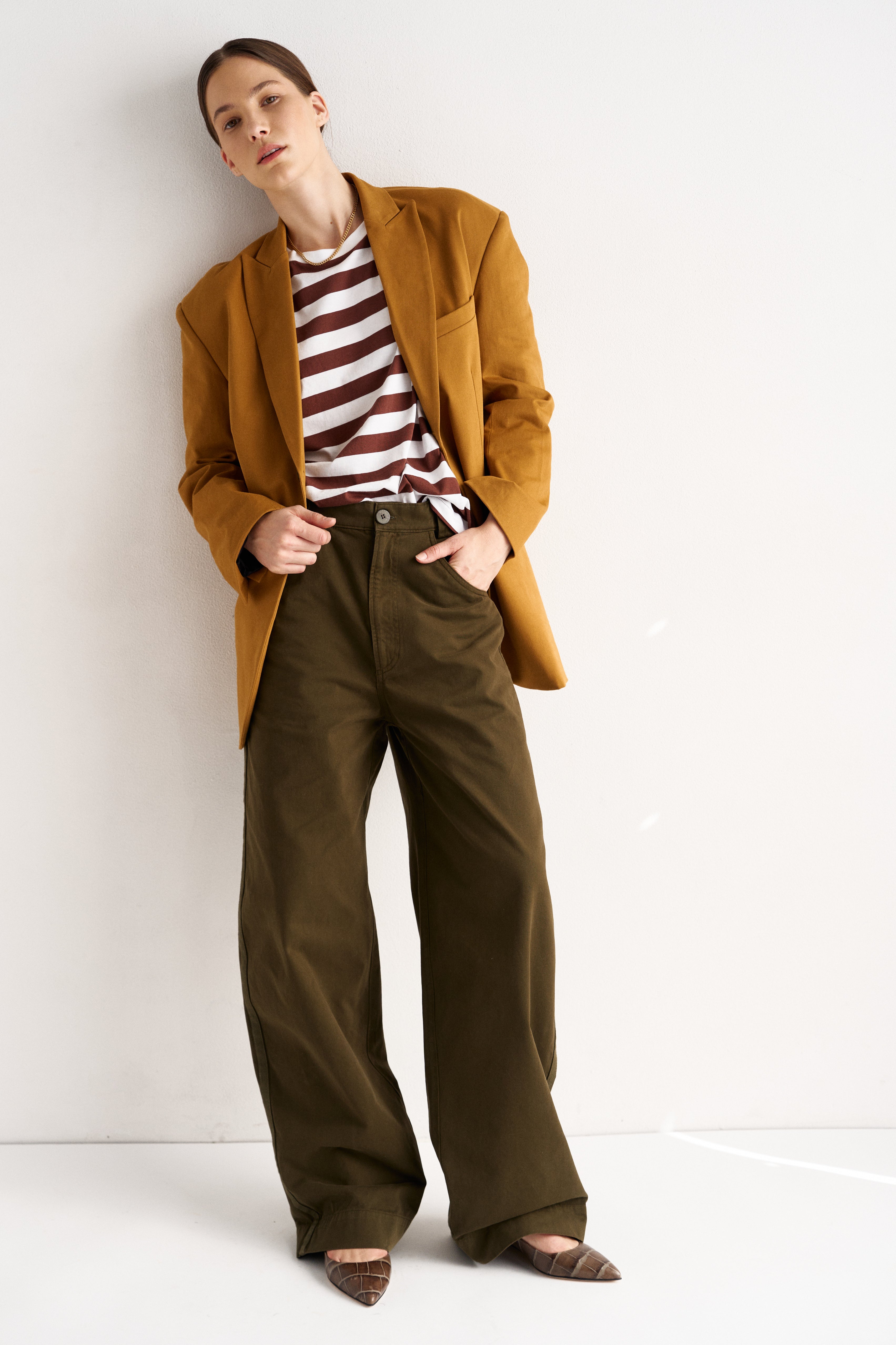 Person wearing a mustard yellow coat, striped shirt, and green pants on a white background