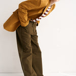 Woman wearing a mustard yellow shirt and green pants on a white background