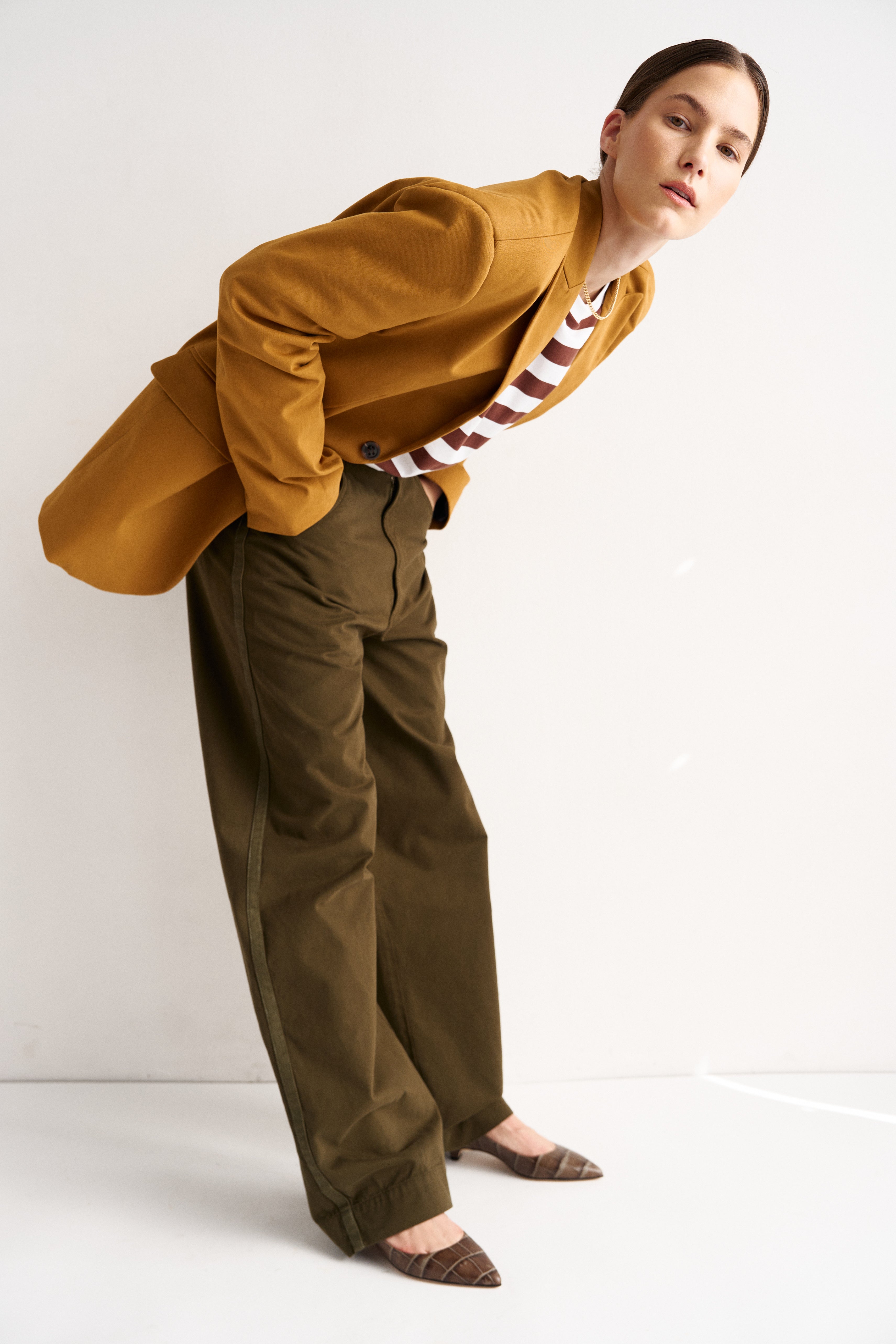 Woman wearing a mustard yellow shirt and green pants on a white background
