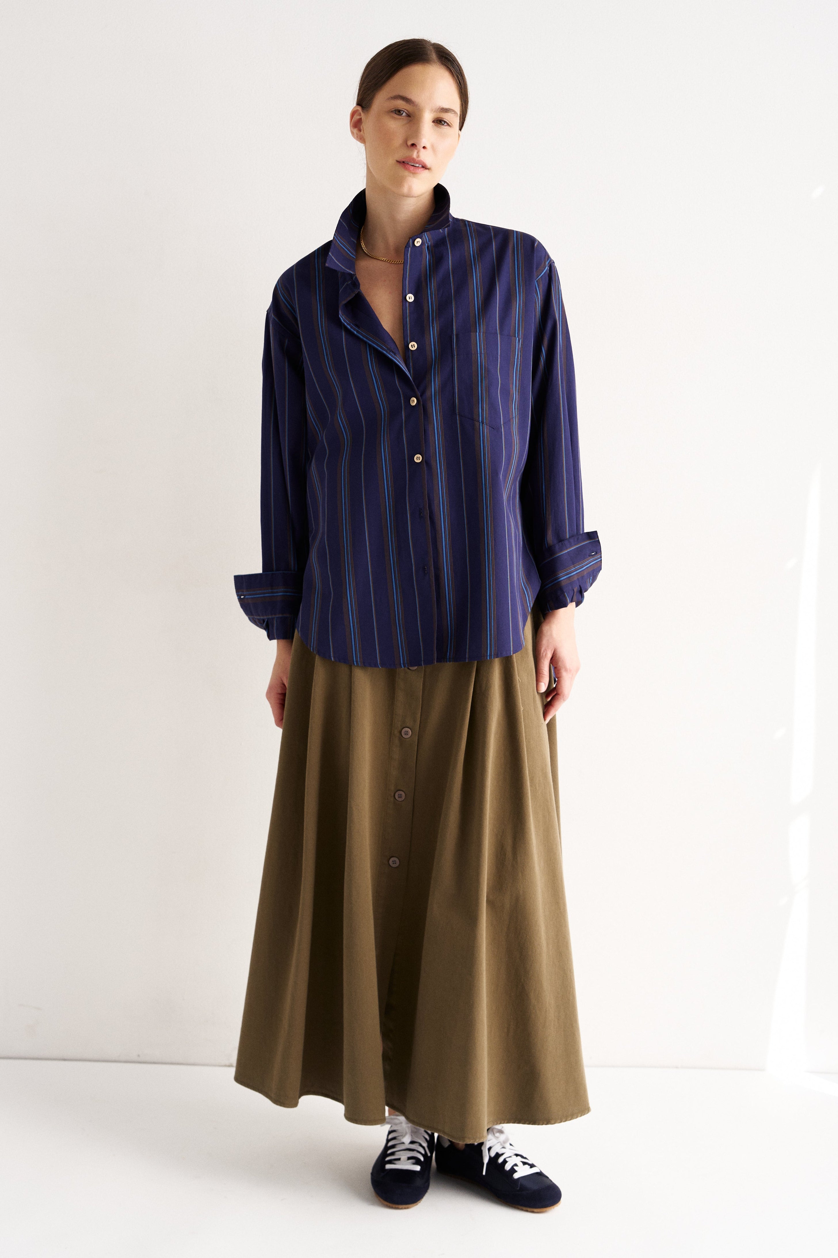 Woman wearing a navy striped shirt and brown skirt on a white background