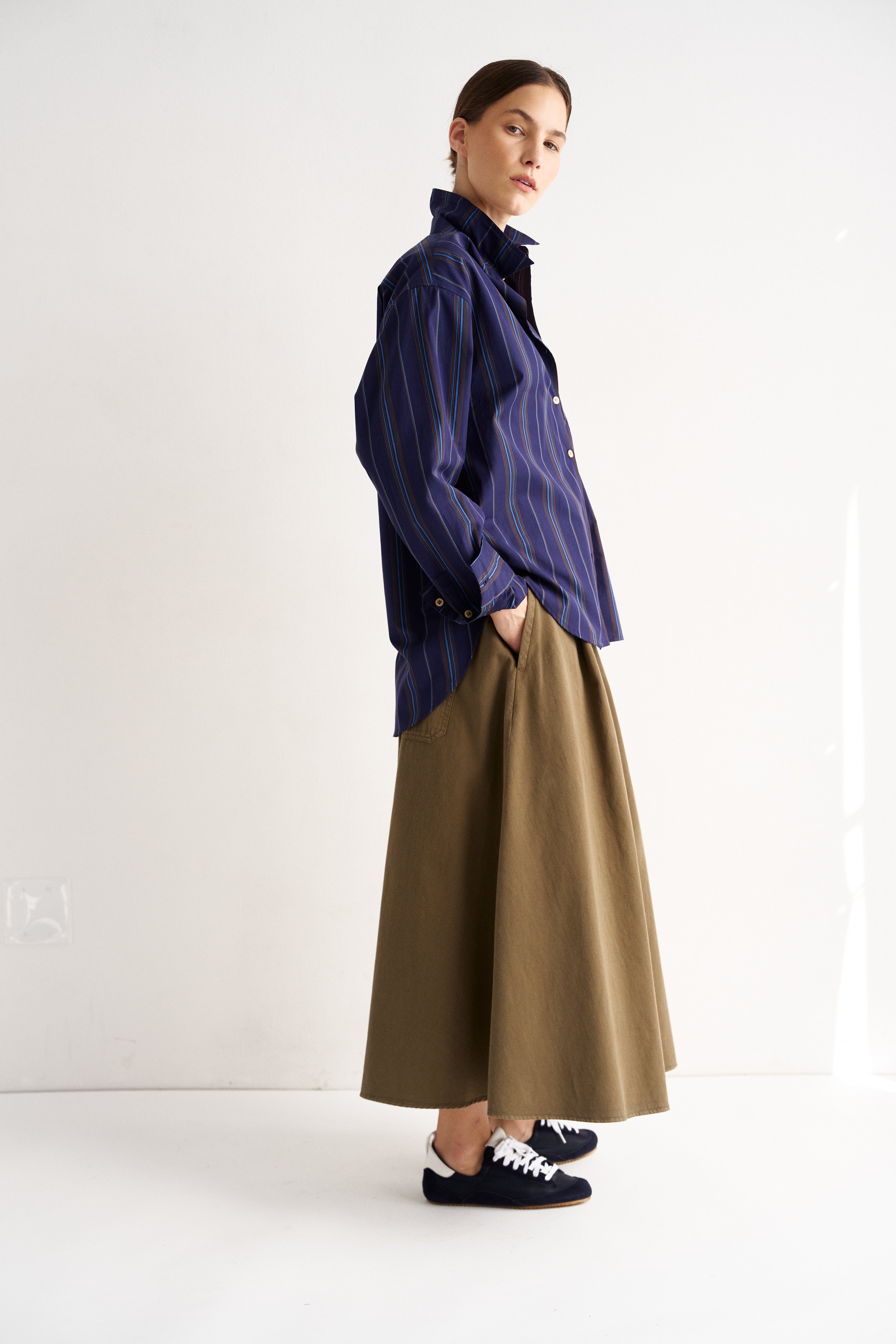 Person wearing a blue shirt and brown skirt on a white background